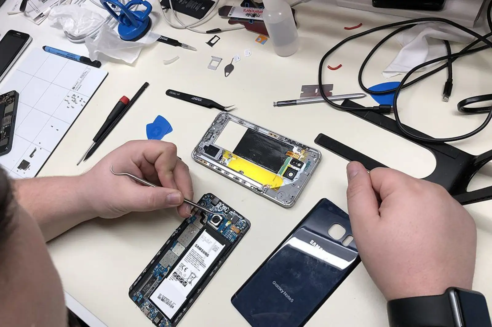 Um Samsung Galaxy desmontado na bancada, com a tampa traseira ao lado, pinça e ferramentas.