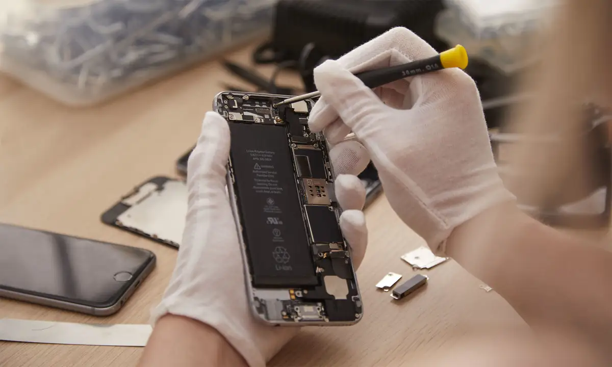 Mãos de luva branca soltam com uma chave de precisão a bateria de um iPhone aberto.